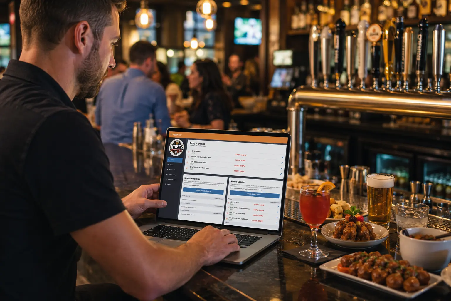 A bar manager uses the AppyHour Business Profile platform on a laptop while seated at a busy neighborhood bar. Drinks, appetizers, and draft beer taps surround the workspace as guests socialize in the background, illustrating hospitality operators managing specials, promotions, and venue visibility.